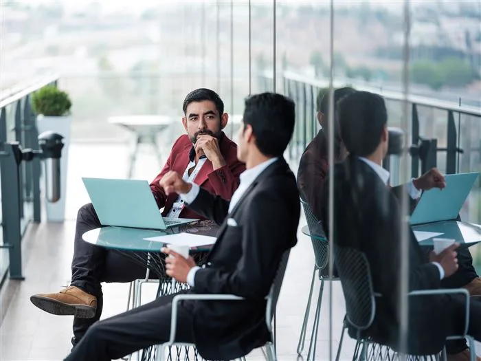Two professionals working with laptops in a glass-walled lounge