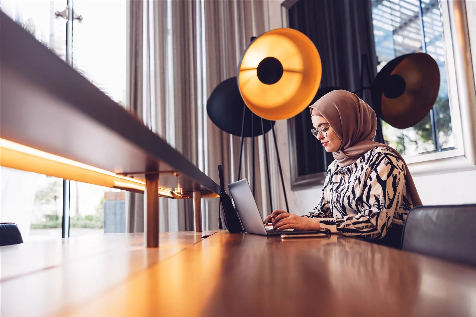 Woman working on a laptop at a long wooden table